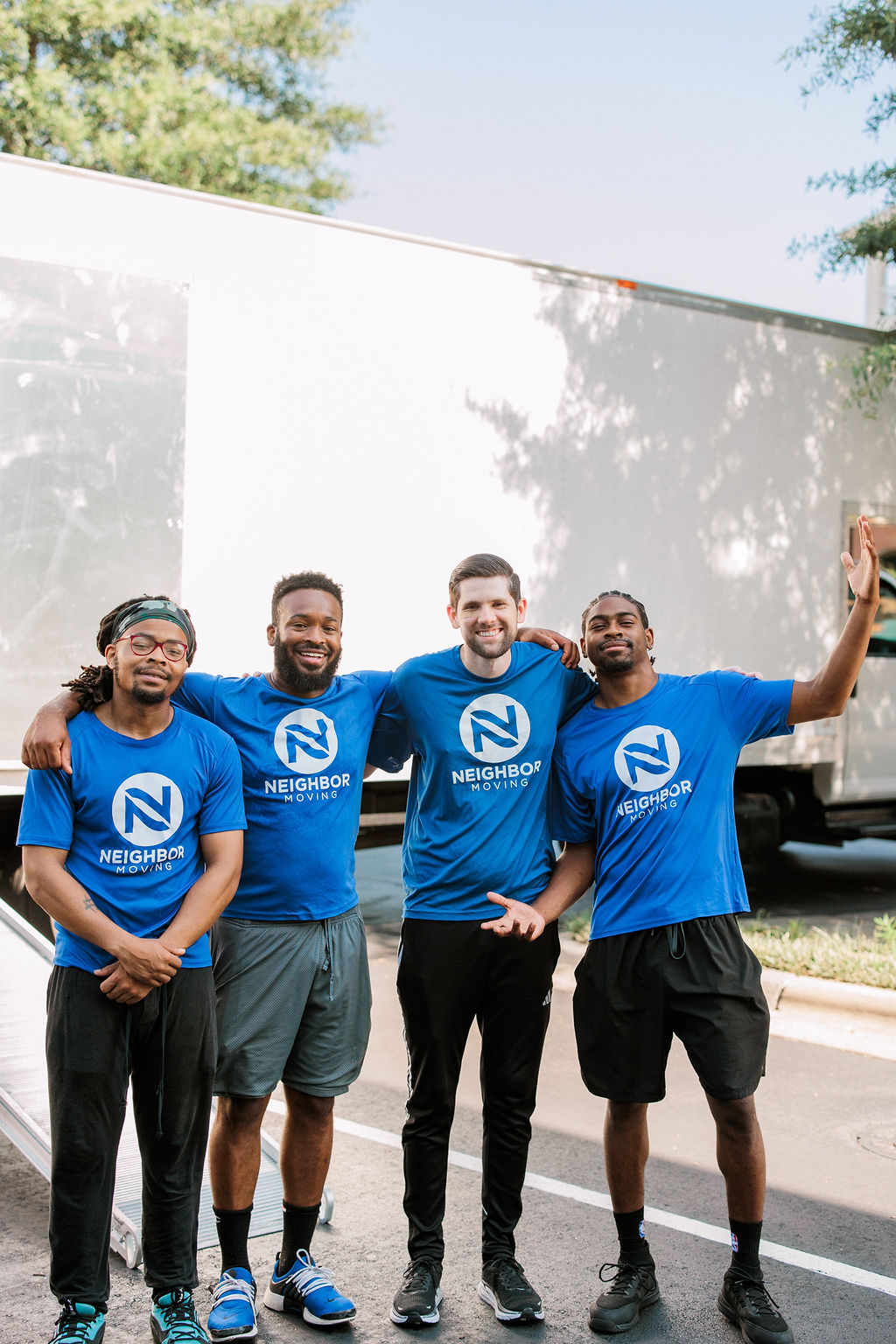 Four moving crew members standing in front of a moving truck waving